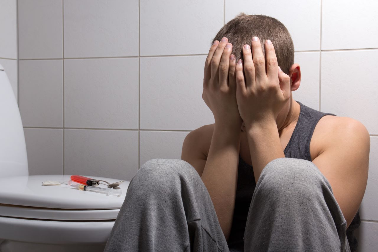 young stoned man with heroin addiction sitting in bathroom